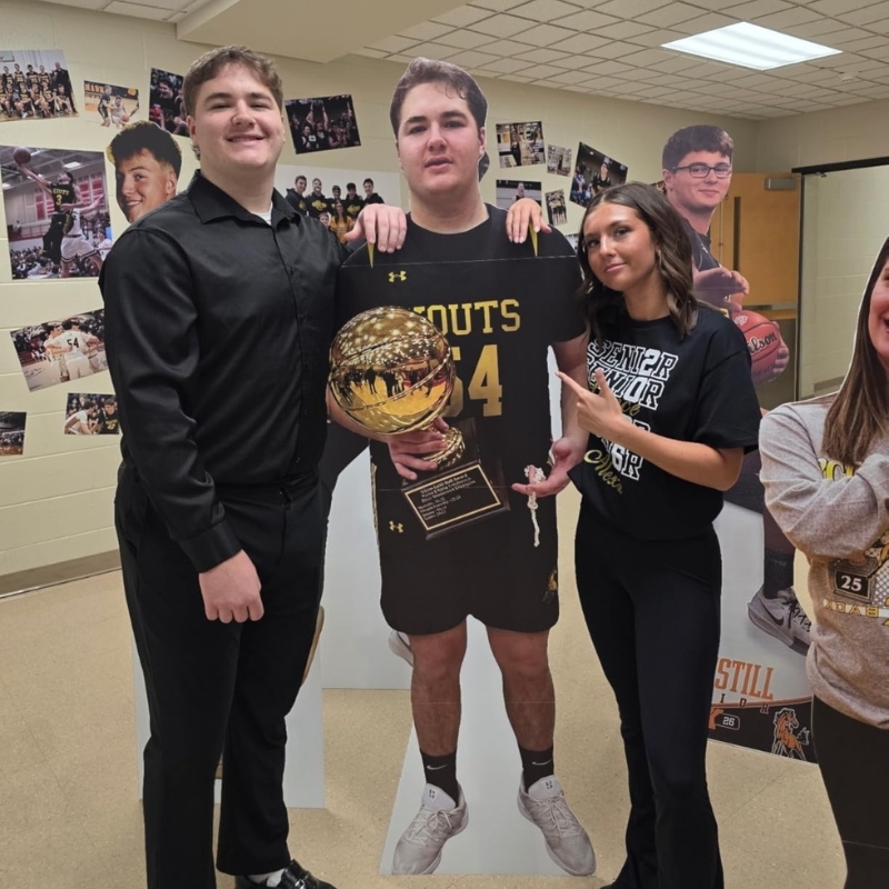 Basketball player life-size cutout holding championship trophy with friends posing