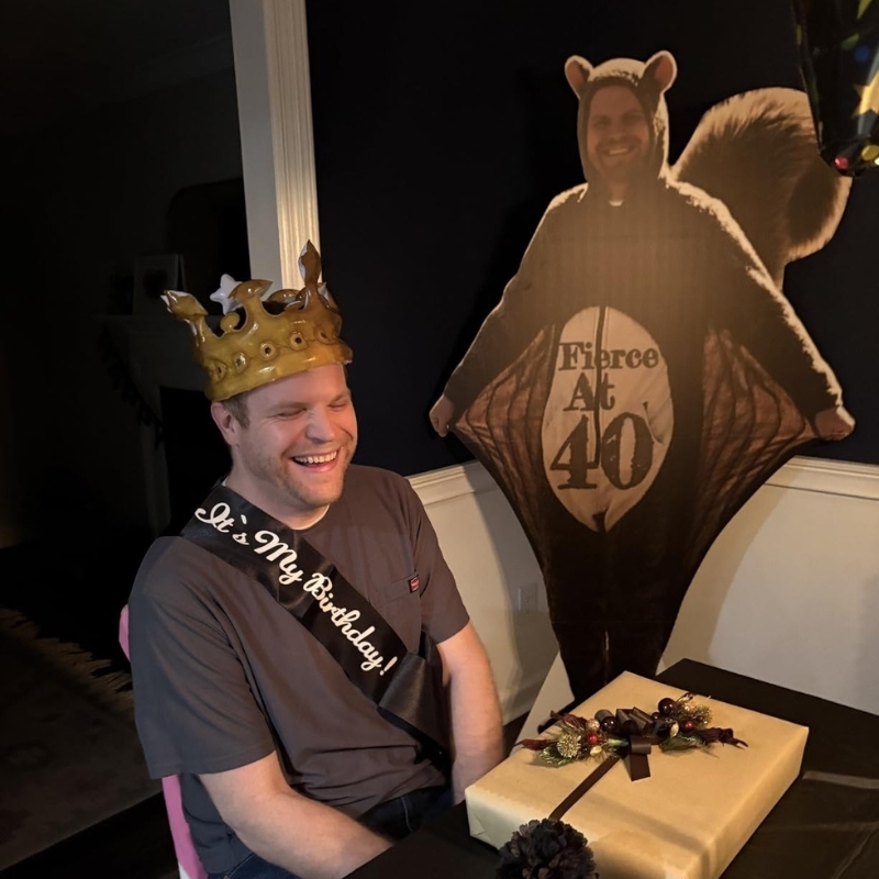 Man wearing birthday crown next to flying squirrel life-size cutout at 40th birthday party