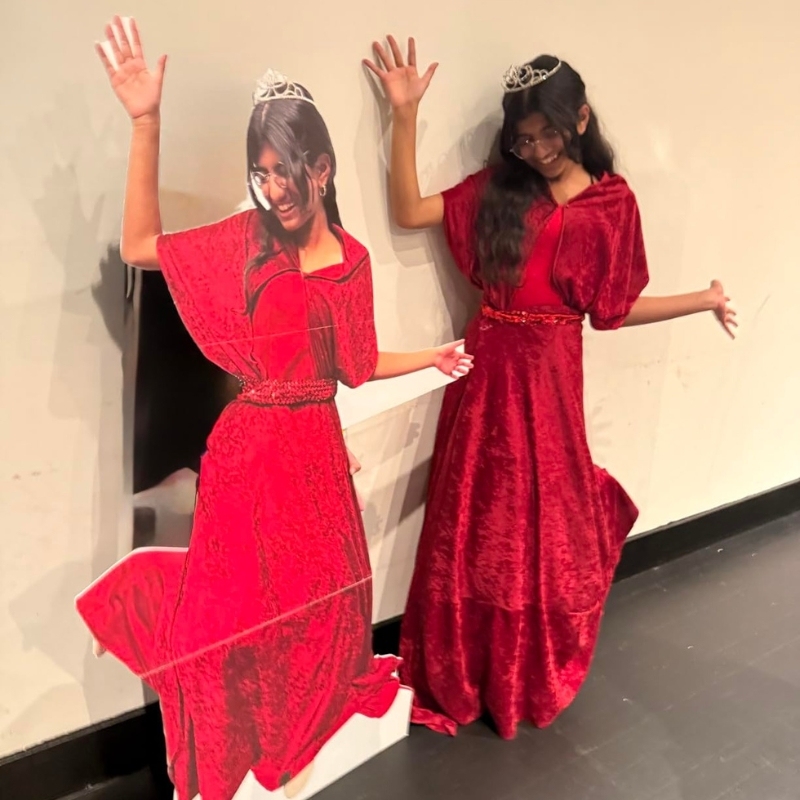 Girl in red velvet dress and tiara posing with her life-size cutout twin