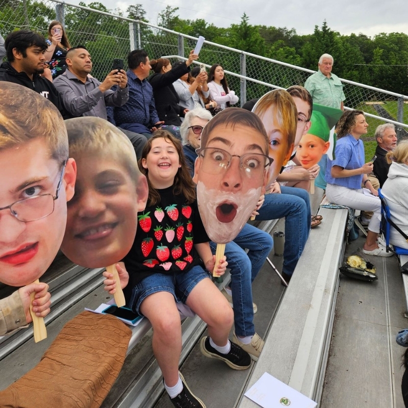 Crowd cheering with big head cutouts on sticks at stadium bleachers