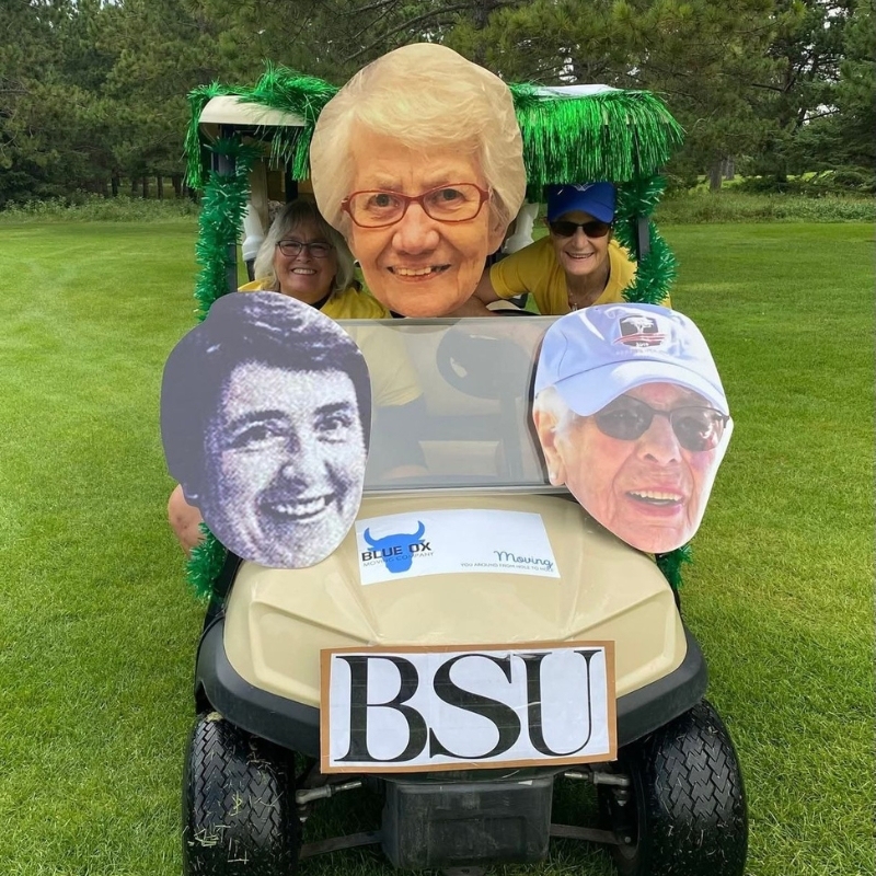 Golf cart decorated with multiple big head cutouts on a golf course