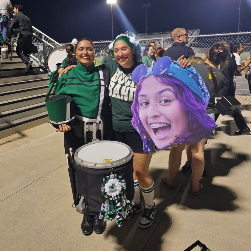 Marching band members at night game holding a big head cutout friend