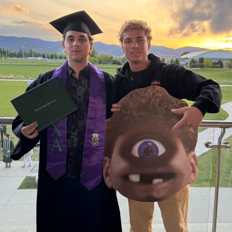 Two graduates at sunset holding a Mike Wazowski big head cutout from Monsters University