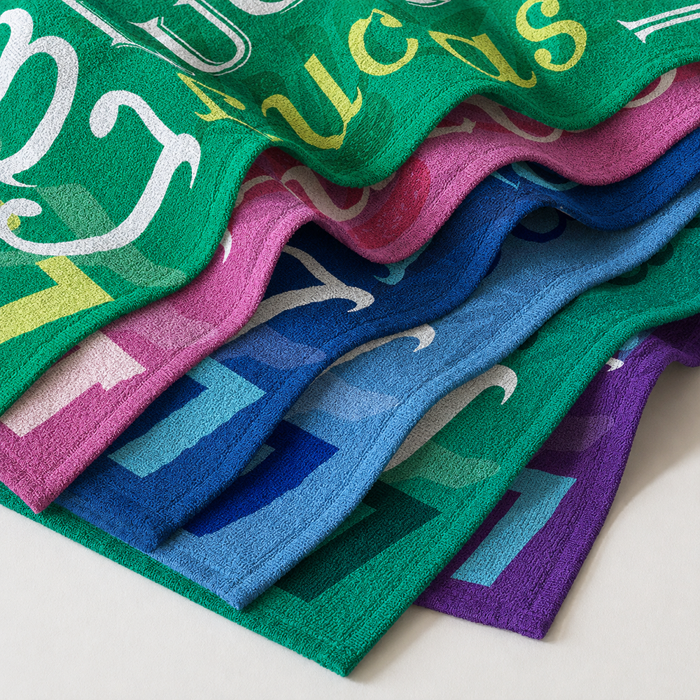 Stacked personalized name collage beach towels in multiple colors showing soft microfiber material and custom patterns