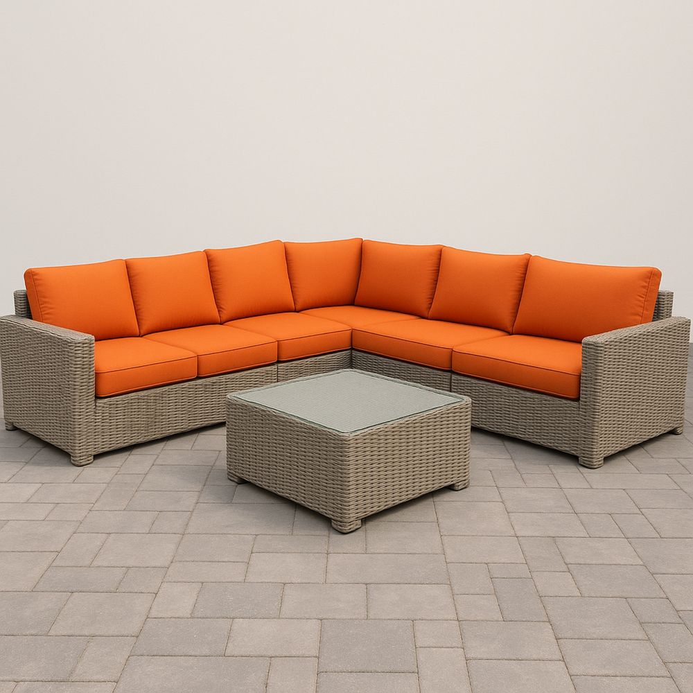 Hjørnesofa i rotting med oransje puter og glassbord