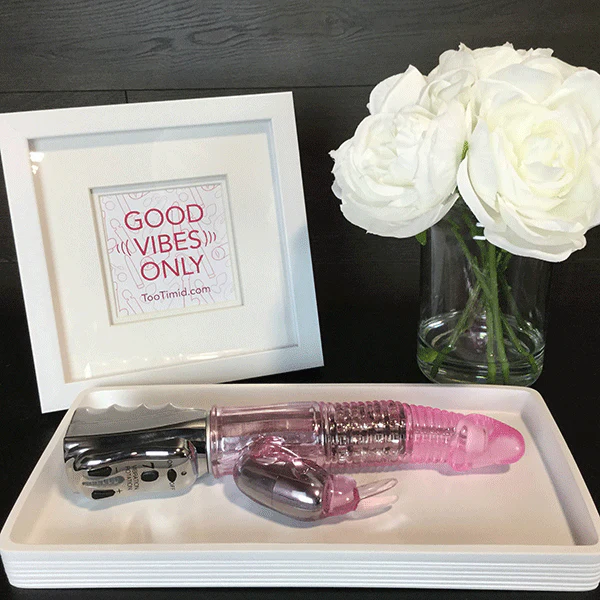 Rotating best selling dual-action rabbit vibe laying on table next to white flowers 