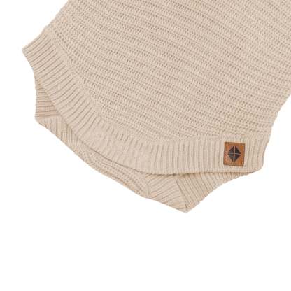 Close up of the snap closure on the Chunky Knit Romper in Almond with the Kyte Baby Vegan leather tag visible