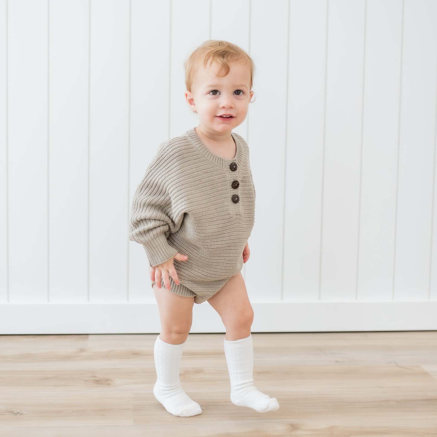 Toddler walking wearing the Chunky Knit Romper in Almond and Cloud Knee high socks
