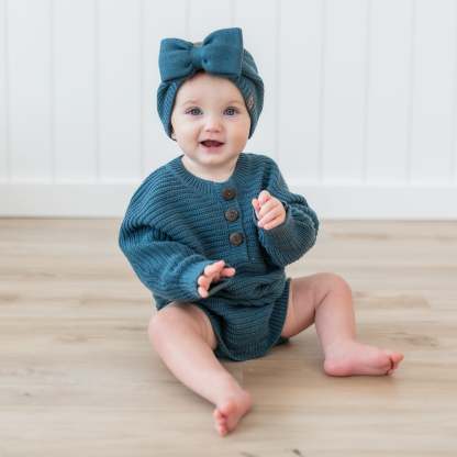 Toddler sitting on the floor wearing the Chunky Knit Romper in Atlantic paired with a Chunky knit bow headband