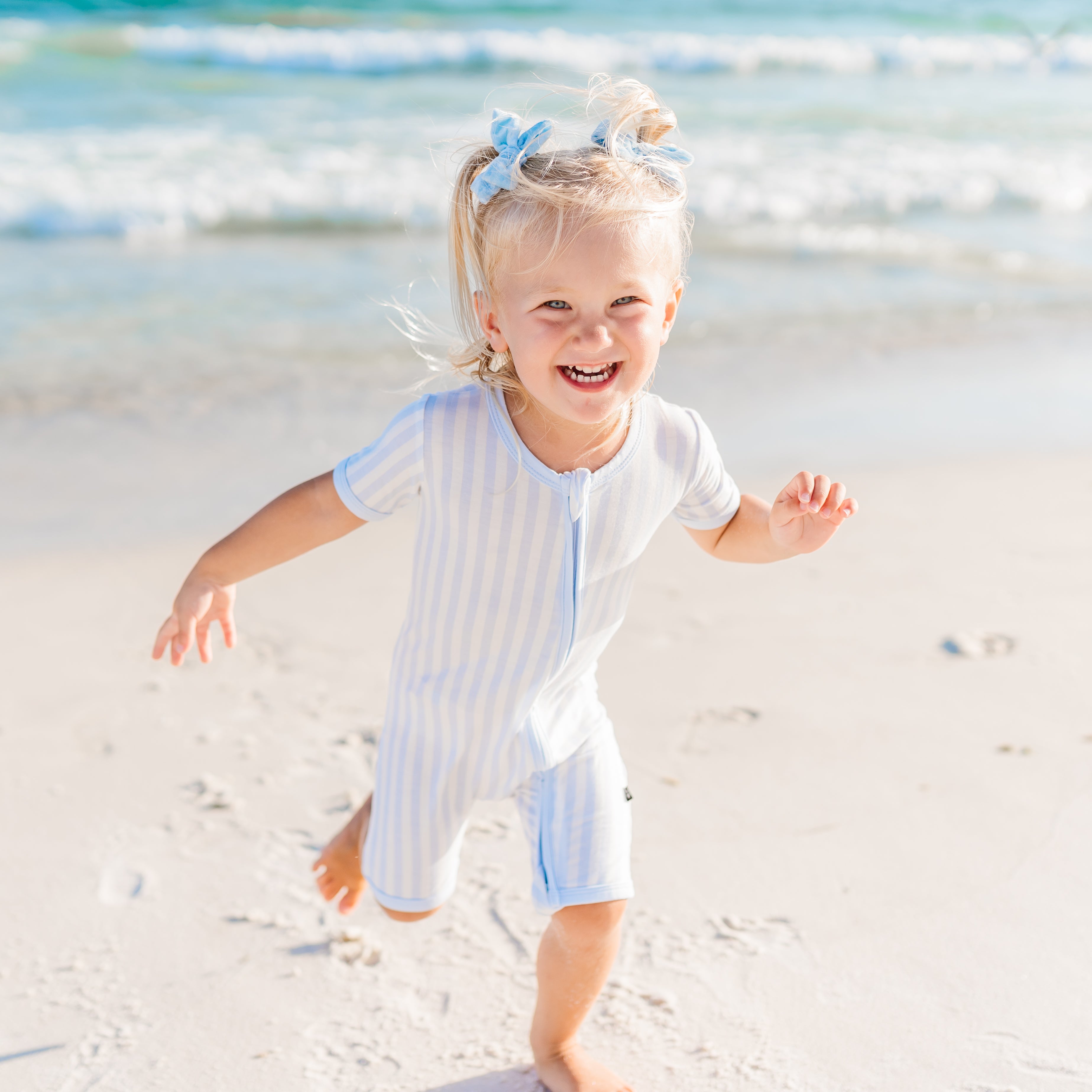Toddler wearing mist stripe zipper shortall running on the beach