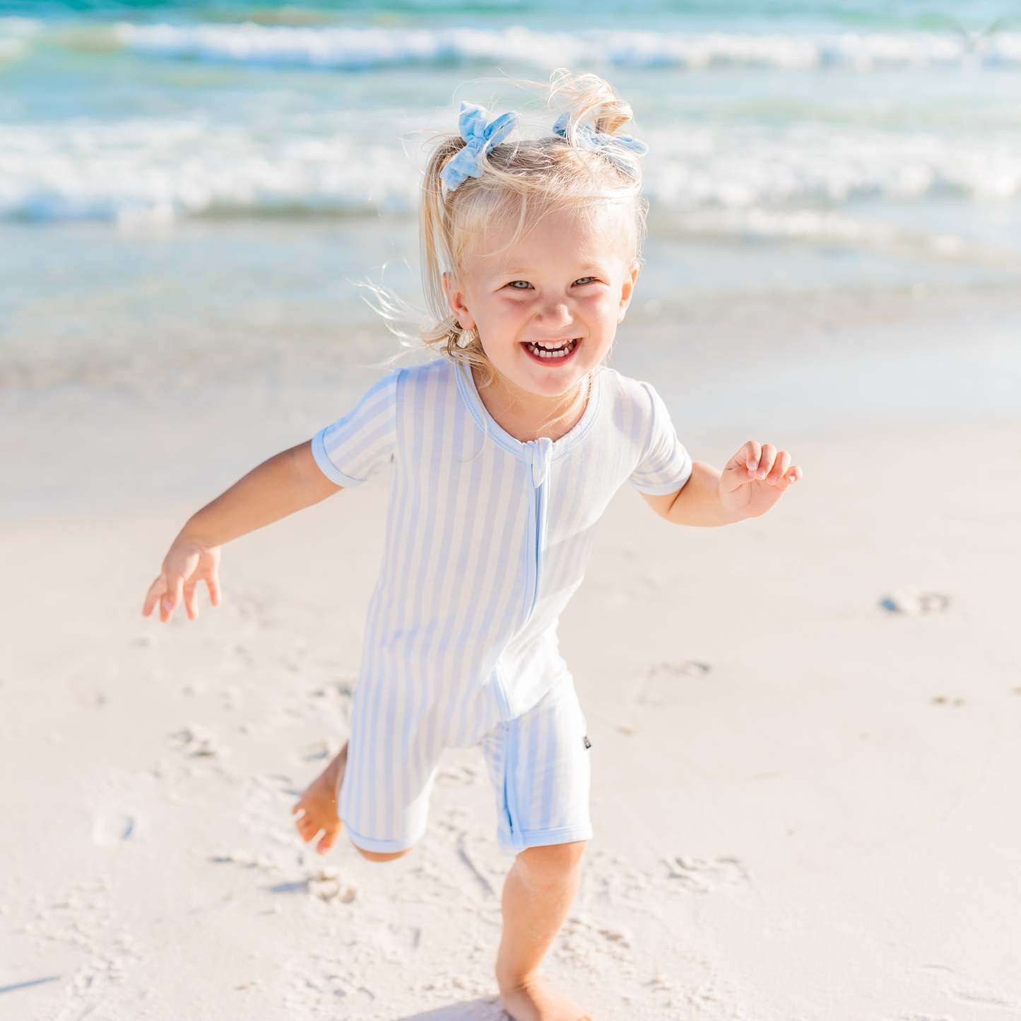 Toddler wearing mist stripe zipper shortall running on the beach