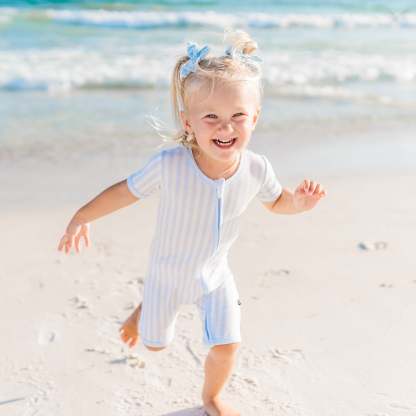 Toddler wearing mist stripe zipper shortall running on the beach