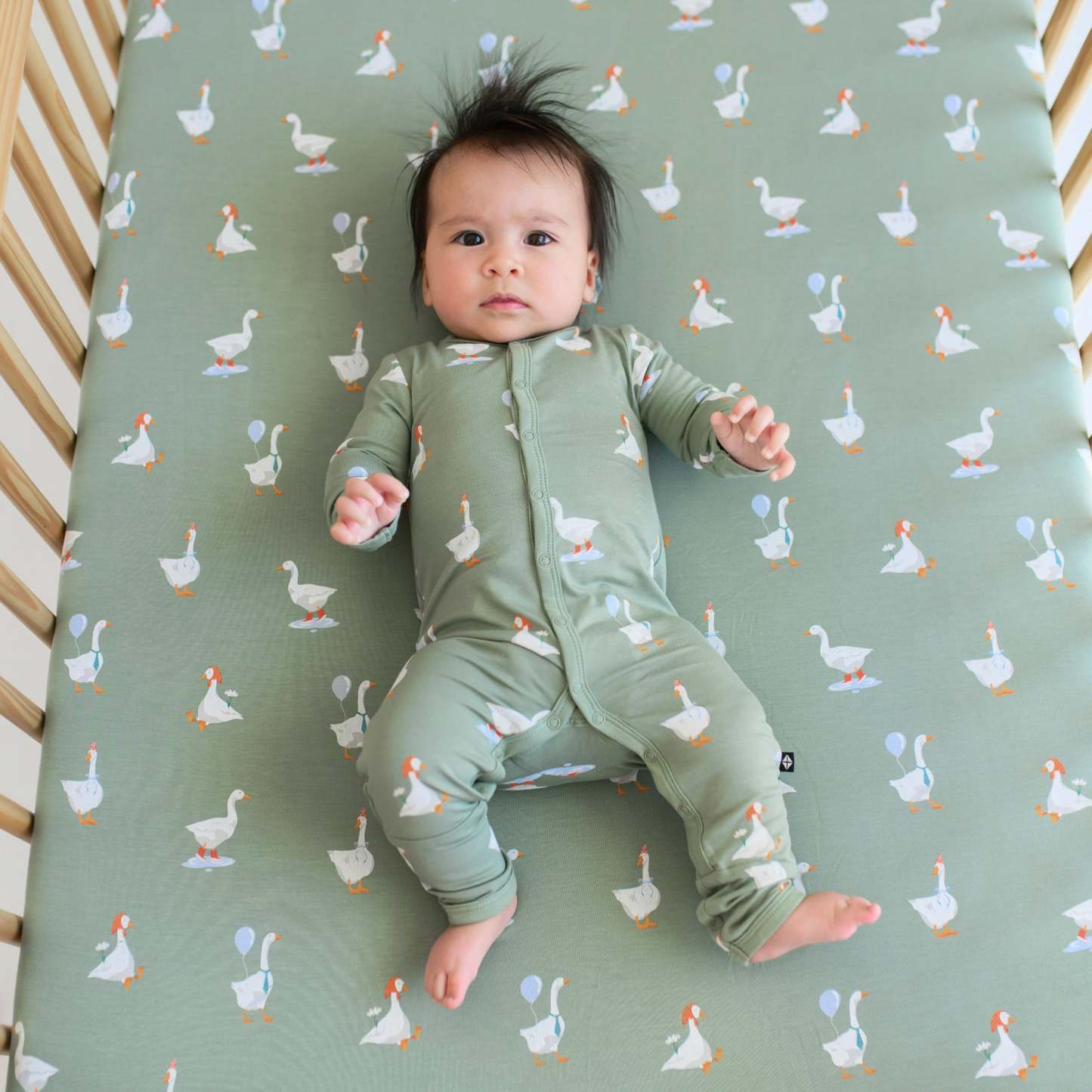 Infant wearing Silly Goose snap romper laying on matching goose crib sheet