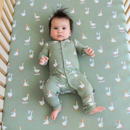Infant wearing Silly Goose snap romper laying on matching goose crib sheet
