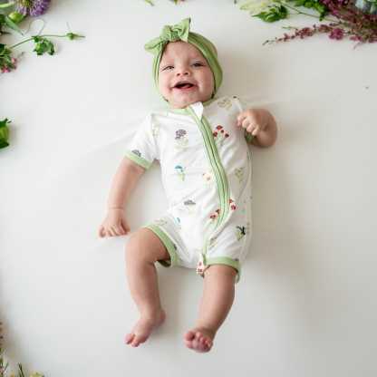 Baby smiling wearing Zippered Shortall Romper in Wildflower and Honu bow