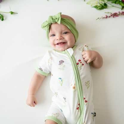 Close up of Baby smiling wearing Zippered Shortall Romper in Wildflower and Honu bow