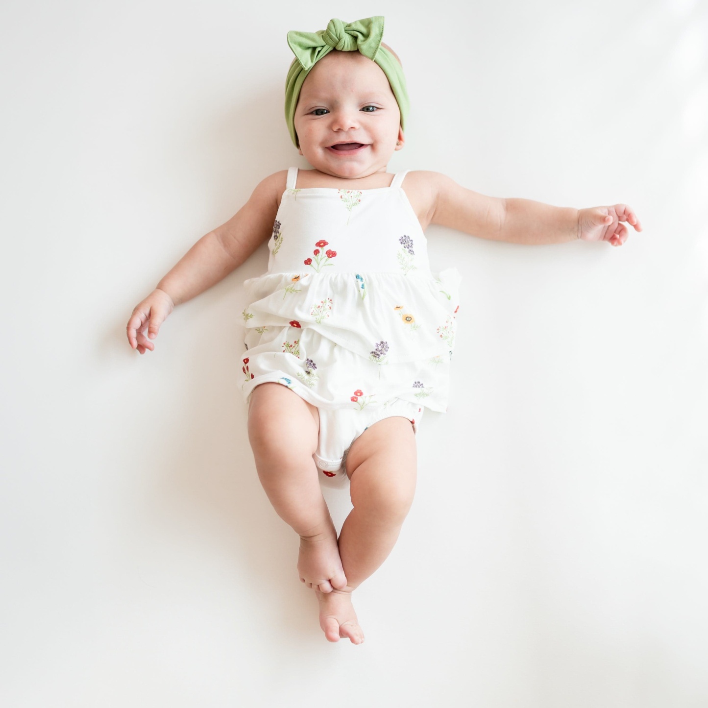 Baby smiling modeling Spaghetti Strap Ruffle Romper in Wildflower and Honu Knotted Headband Bow