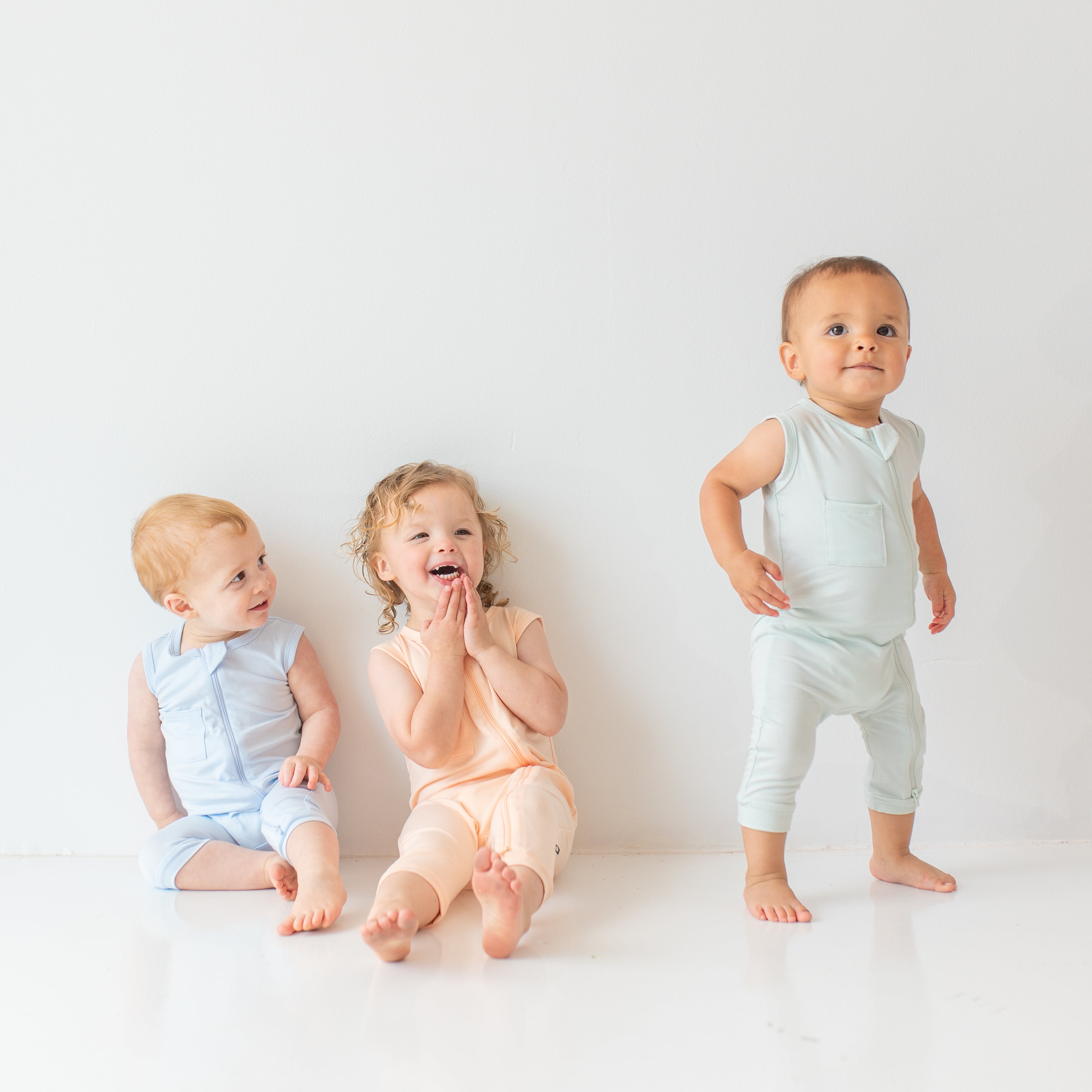 Three toddlers wearing the Zippered Sleeveless Rompers in the Summer Solid colors