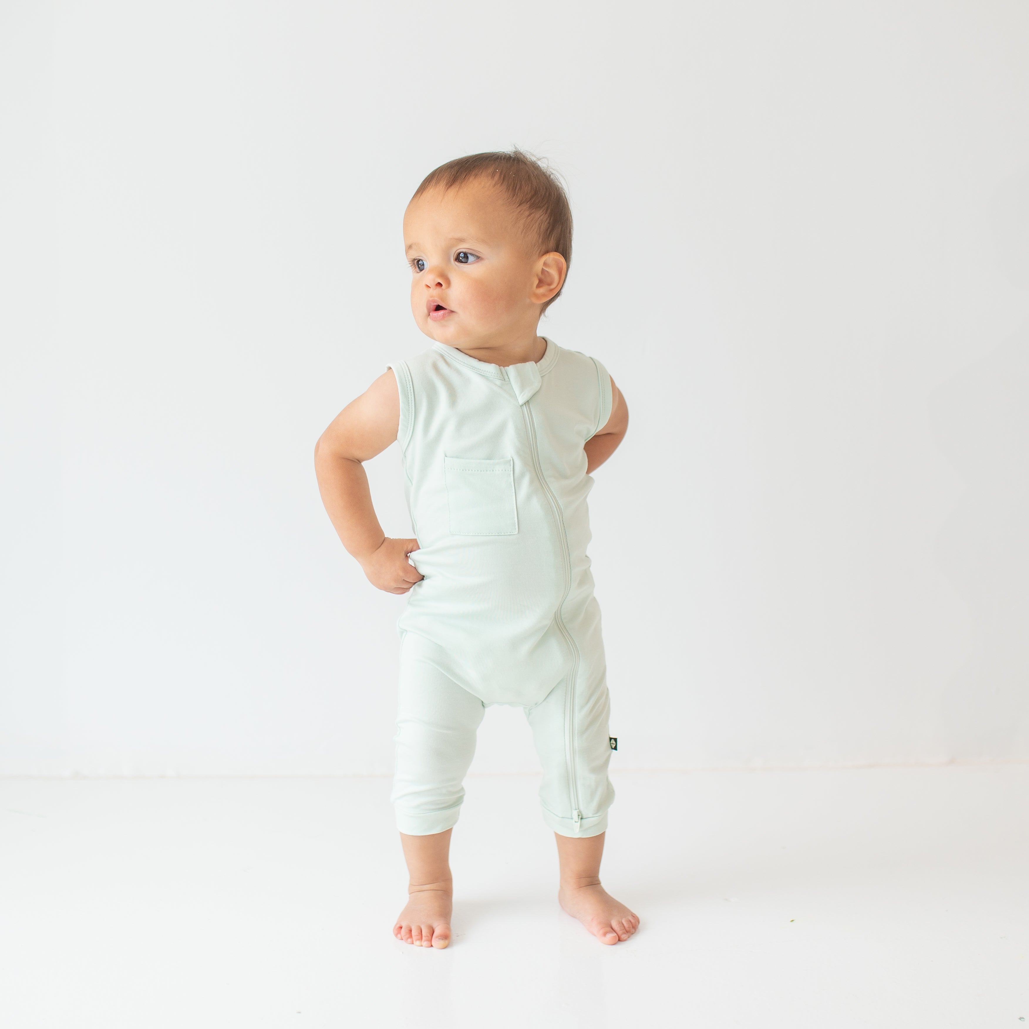 Young toddler model looking off to the side wearing the Zippered Sleeveless Romper in Dew