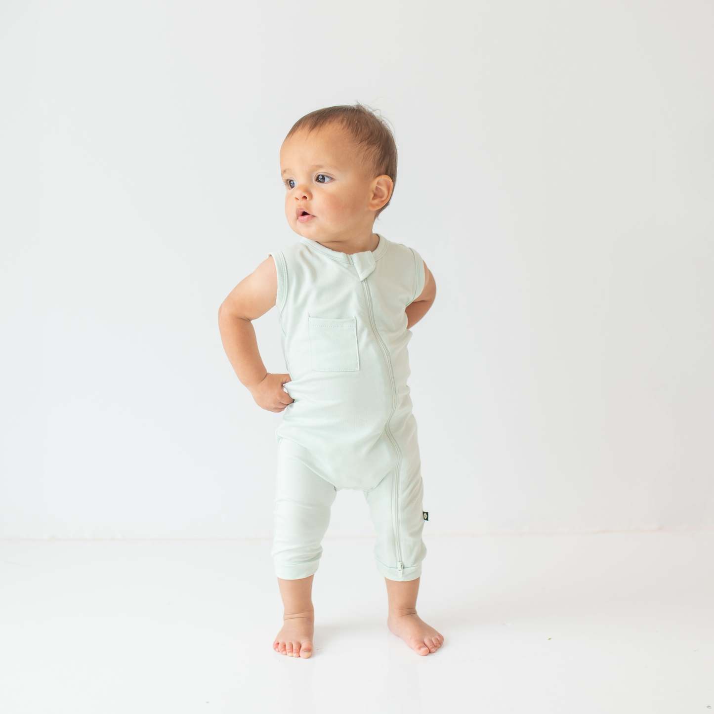 Young toddler model looking off to the side wearing the Zippered Sleeveless Romper in Dew