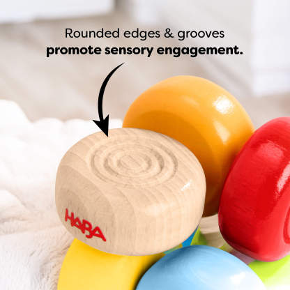 Close up of HABA Color Drops Wooden Grasping and Teething Toy with text reading 'Rounded edges and grooves promote sensory engagement'