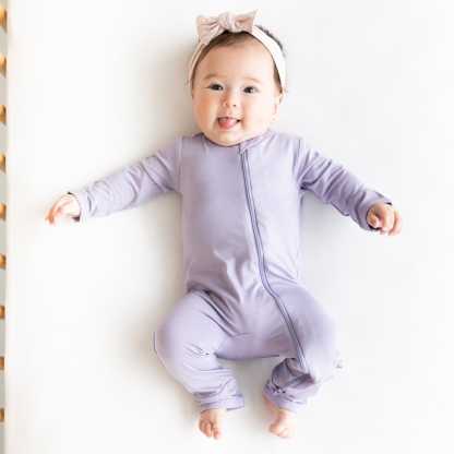 Infant wearing Ziippered Romper in Taro with a headband in Blush