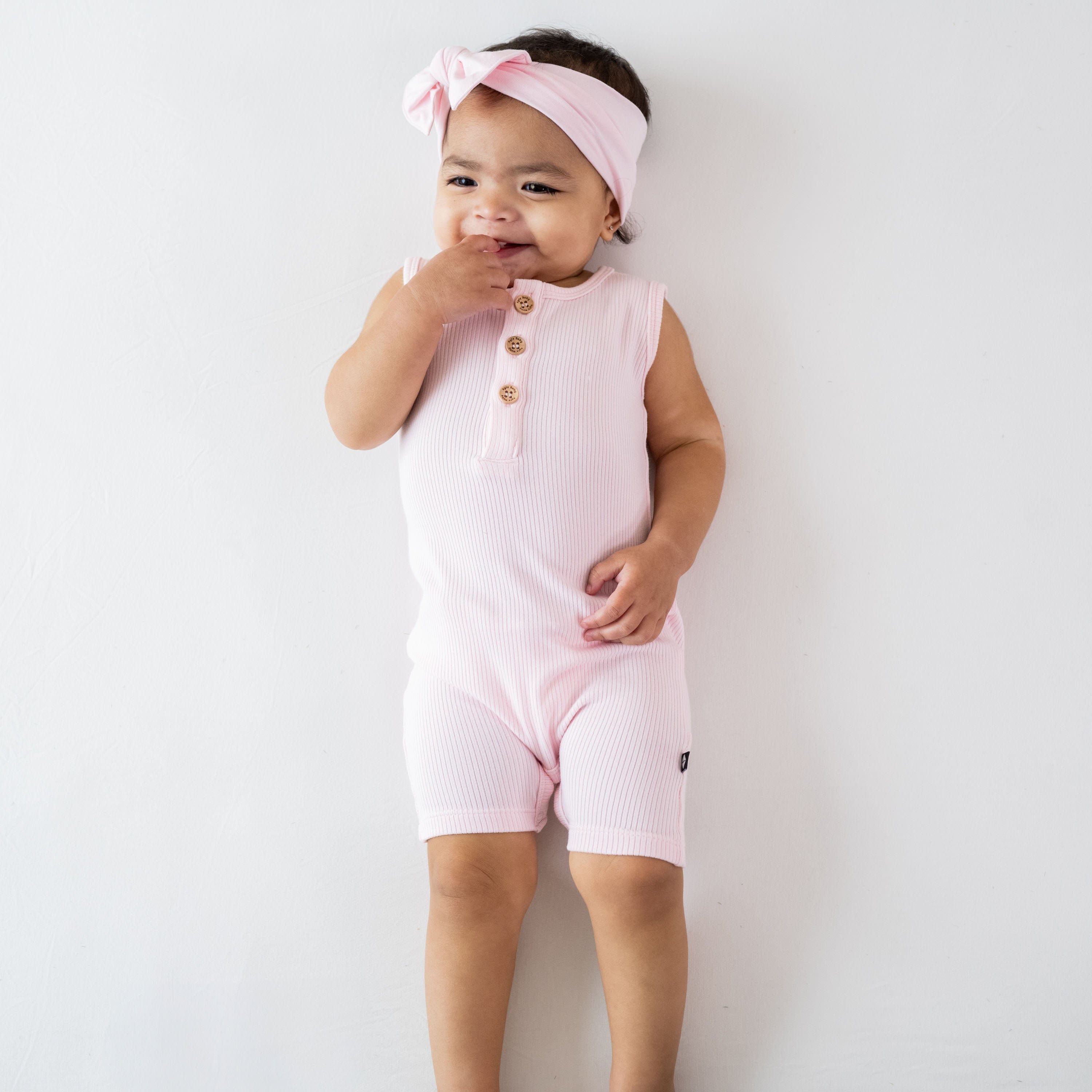 Infant wearing Kyte Baby Ribbed Sleeveless Shortall with wooden buttons in Sakura