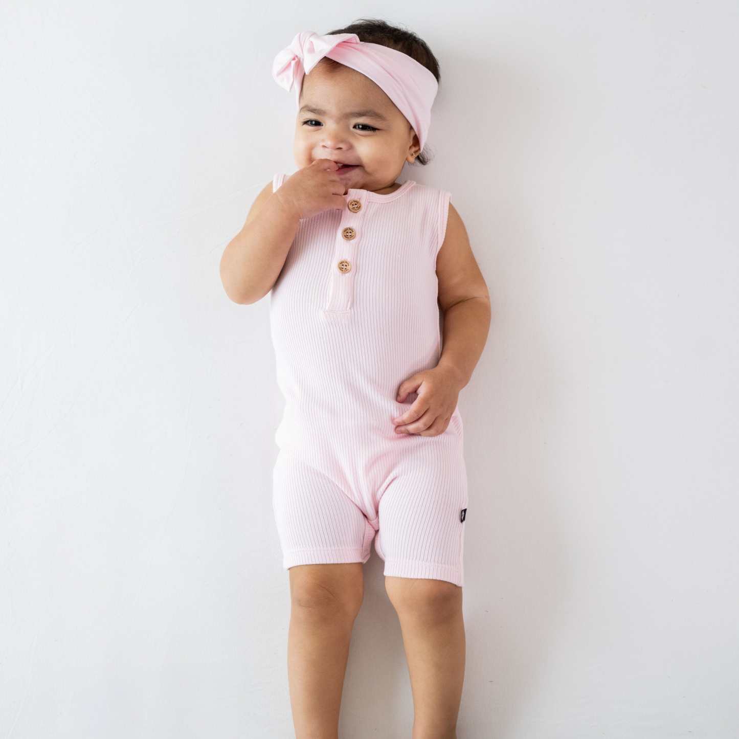 Infant wearing Kyte Baby Ribbed Sleeveless Shortall with wooden buttons in Sakura