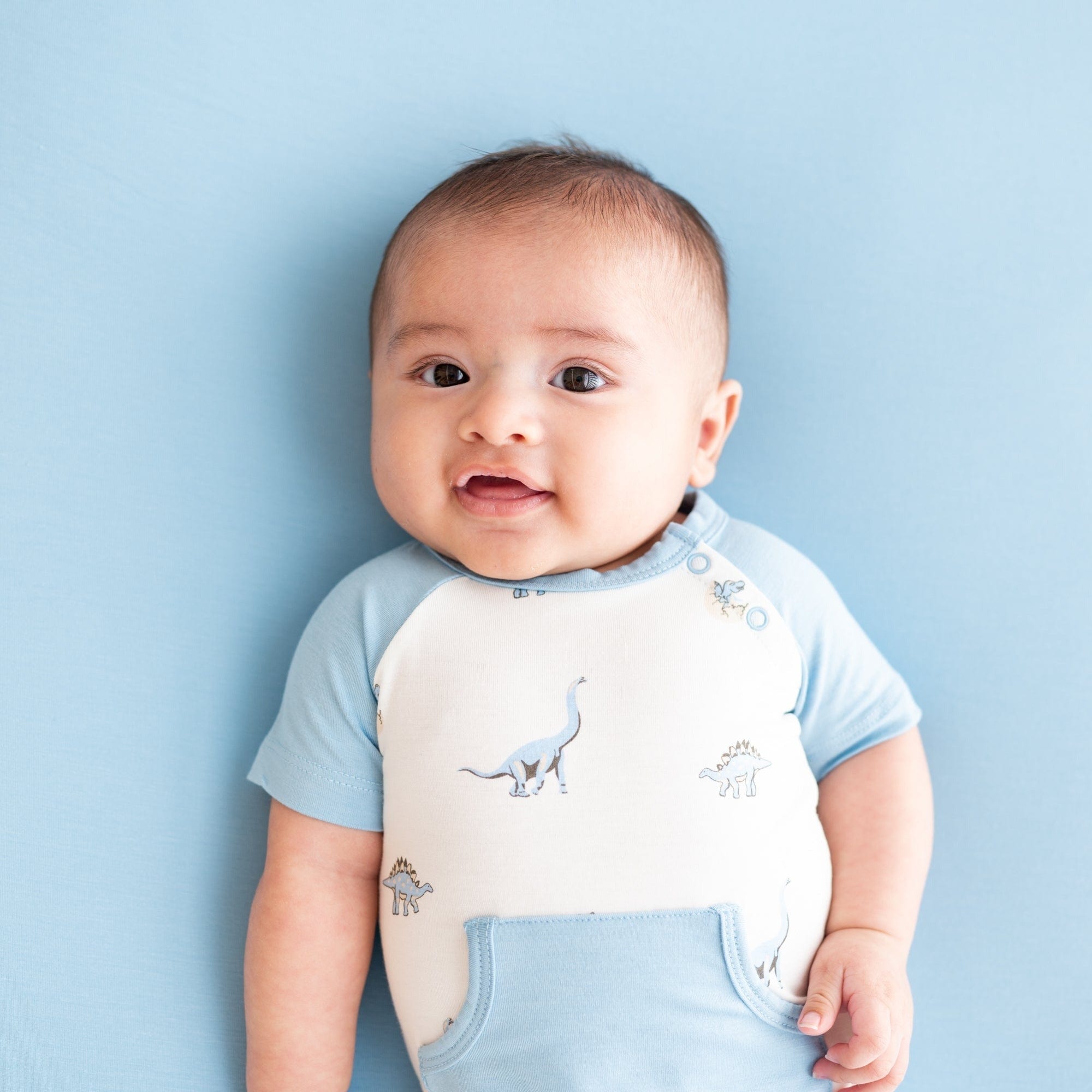 Infant wearing bamboo Kyte Baby Shortall in Jurassic with front pocket