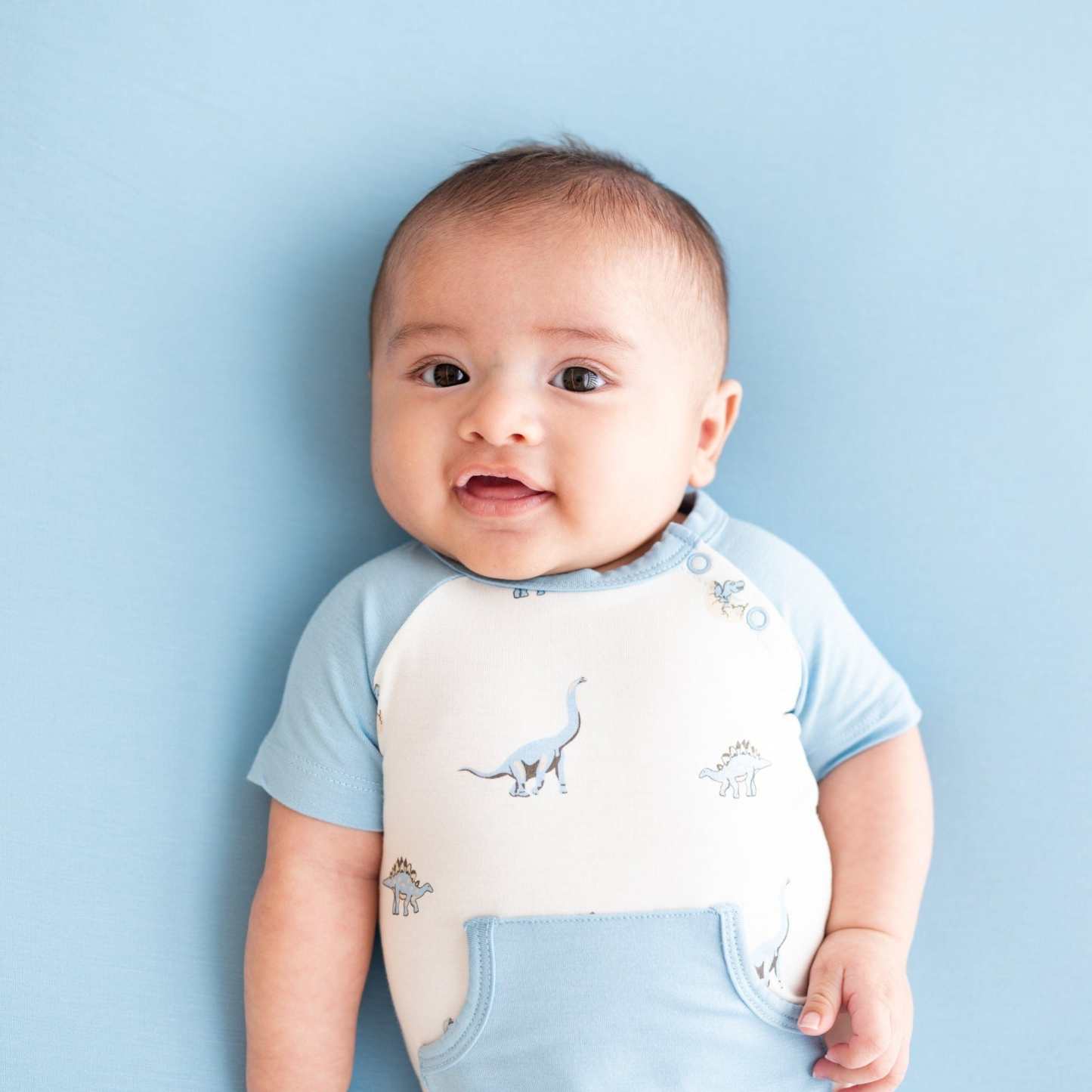 Infant wearing bamboo Kyte Baby Shortall in Jurassic with front pocket