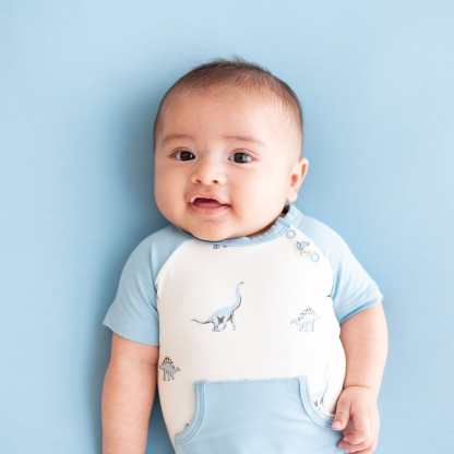 Infant wearing bamboo Kyte Baby Shortall in Jurassic with front pocket