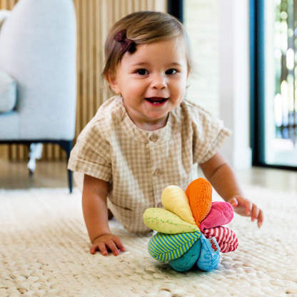 A baby crawling on a light carpet with a colorful, multi-textured ball in front.