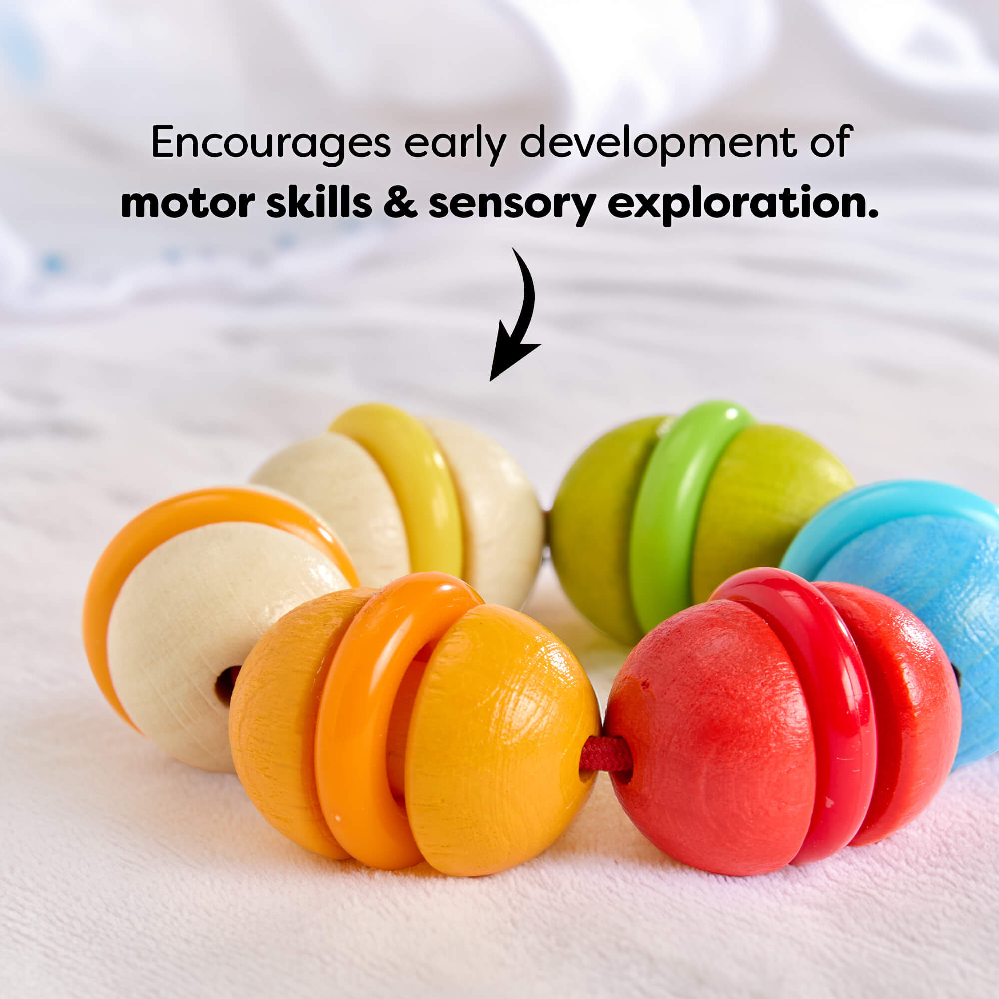 Rainbow Rattle Grasping and Teething Toy wooden baby rattle on a white blanket with text reading 'Encourages early development of motor skills & sensory exploration.'