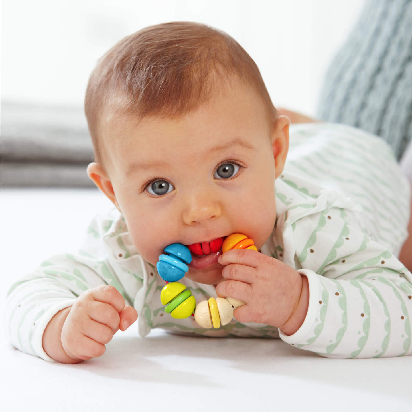 Baby on their tummy playing with a HABA Rainbow Rattle Grasping and Teething Toy