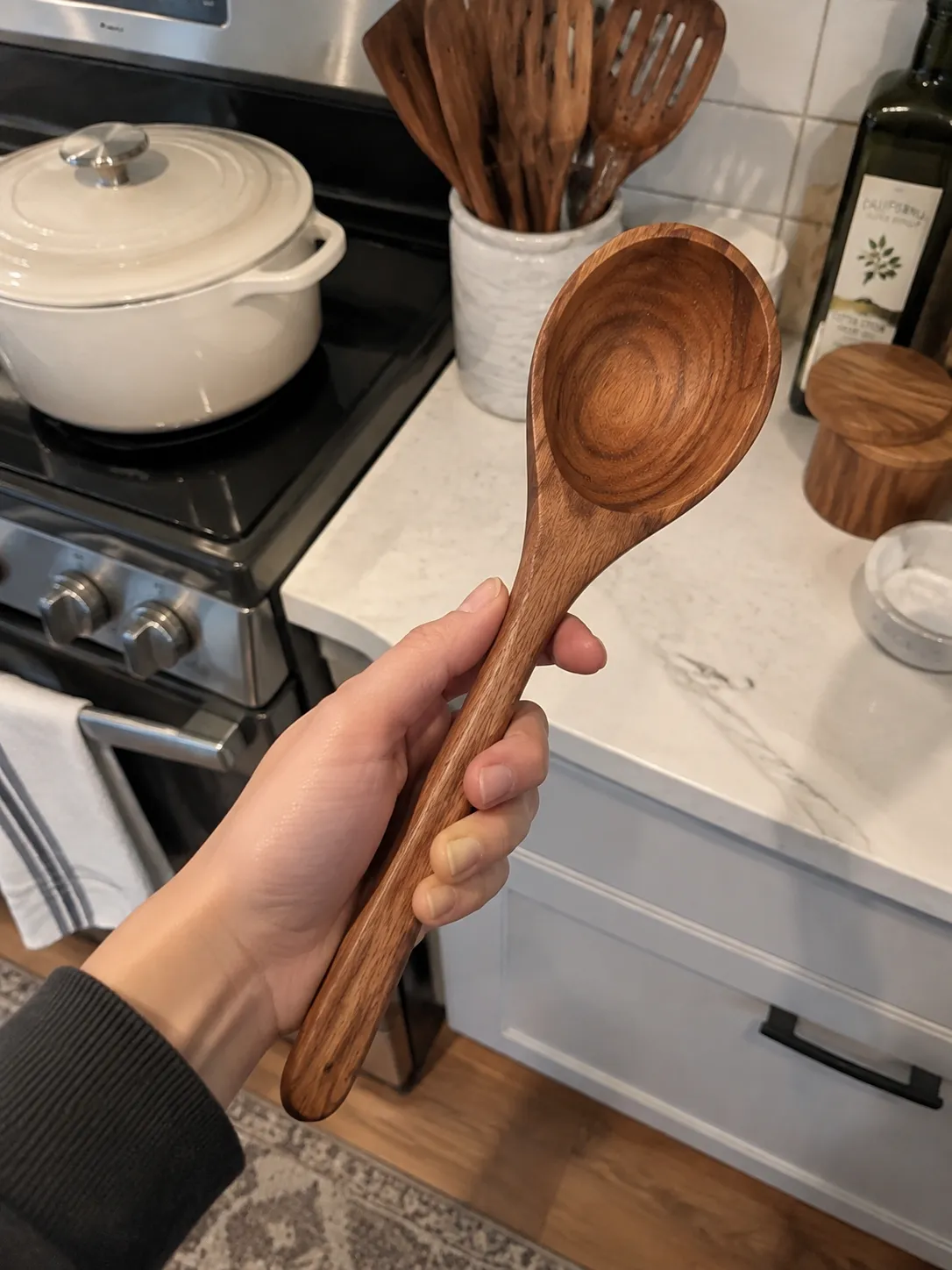 Hand holding an oval wooden spoon in a kitchen
