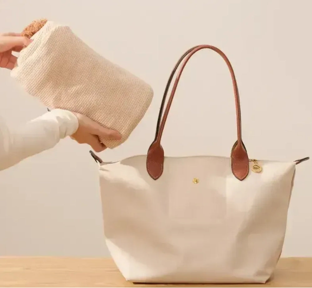 Folded beige shawl being placed into a large tote bag