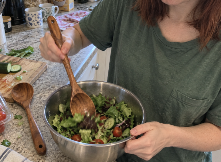 Person mixing salad with a wooden spoon