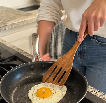 Wooden slotted turner beside a fried egg