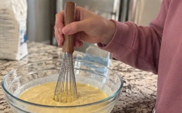 Wood-handled wire whisk mixing eggs in a glass bowl