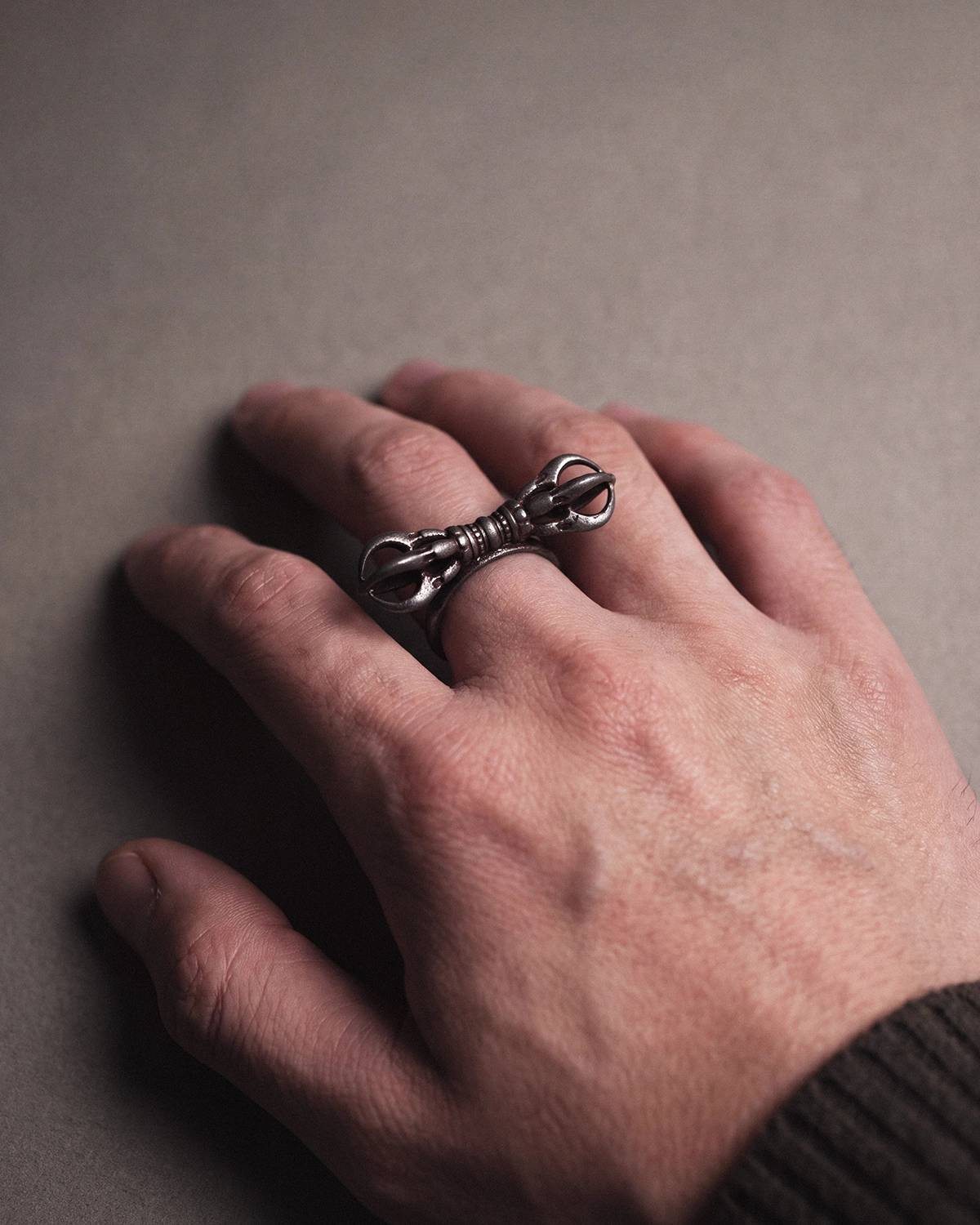 Vajra Dorje cold iron ring worn on a hand resting on a gray surface, with a dark ribbed knit sleeve at the edge of the frame.