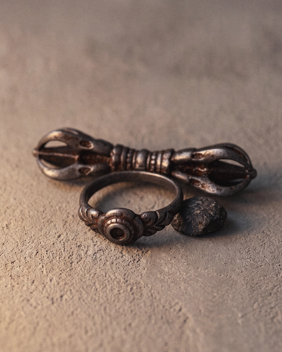 Close-up of the cold iron ring band showing a carved eye motif and lotus-petal relief, with the vajra and a dark stone behind it.