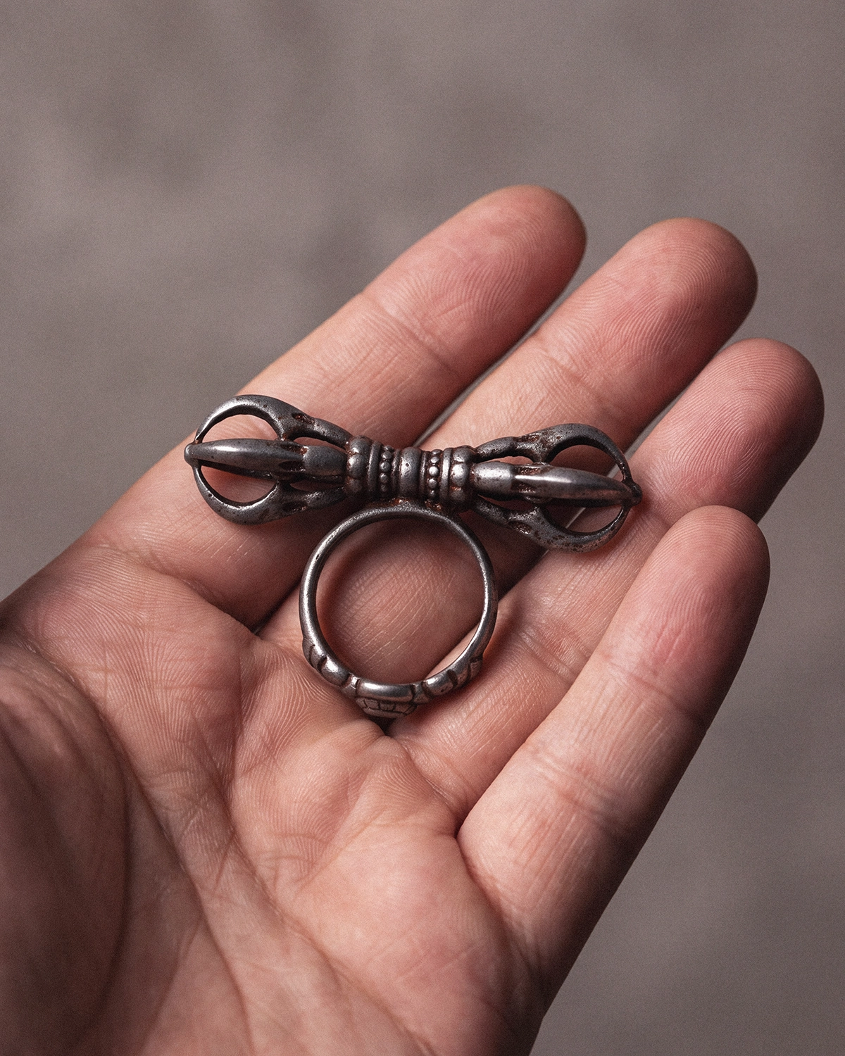 Vajra Dorje cold iron ring resting on an open palm to show its three-pronged form and compact scale.
