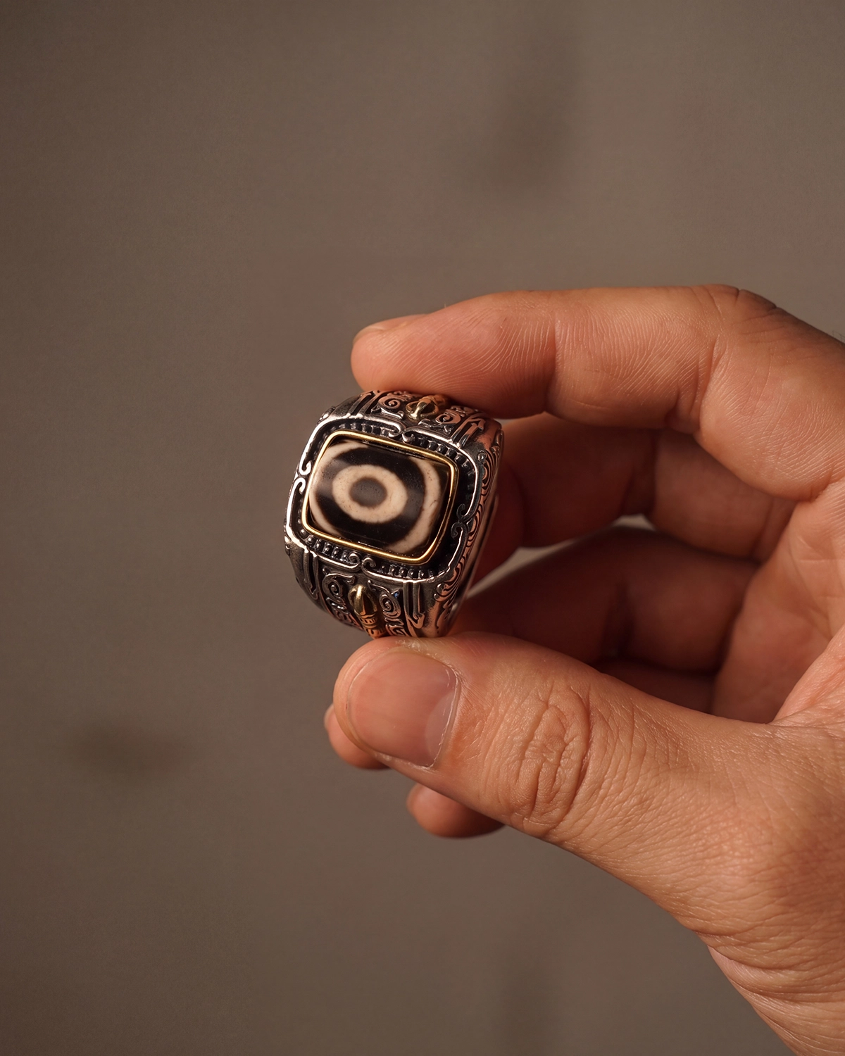 One-eye dzi bead ring held between thumb and forefinger to show its compact size and solid weight.