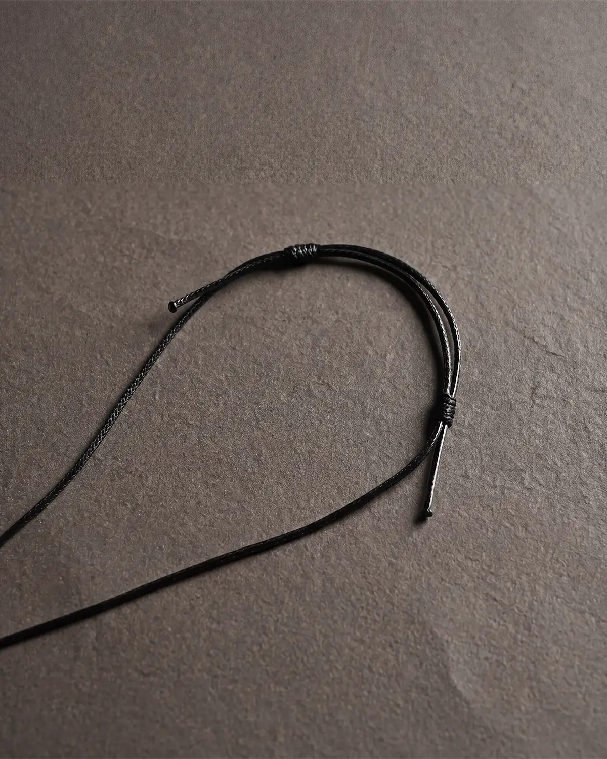 Close-up of a black adjustable necklace cord with a sliding knot laid on a gray textured surface.