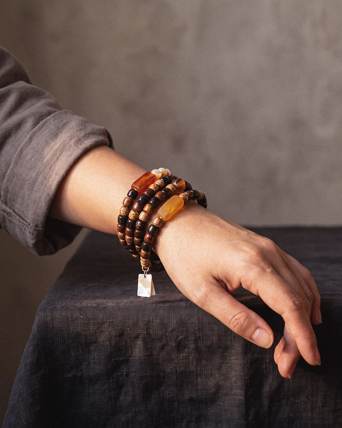Star and moon bodhi seed mala wrapped four times around a wrist, with a gray-brown linen sleeve and a small shell charm visible.