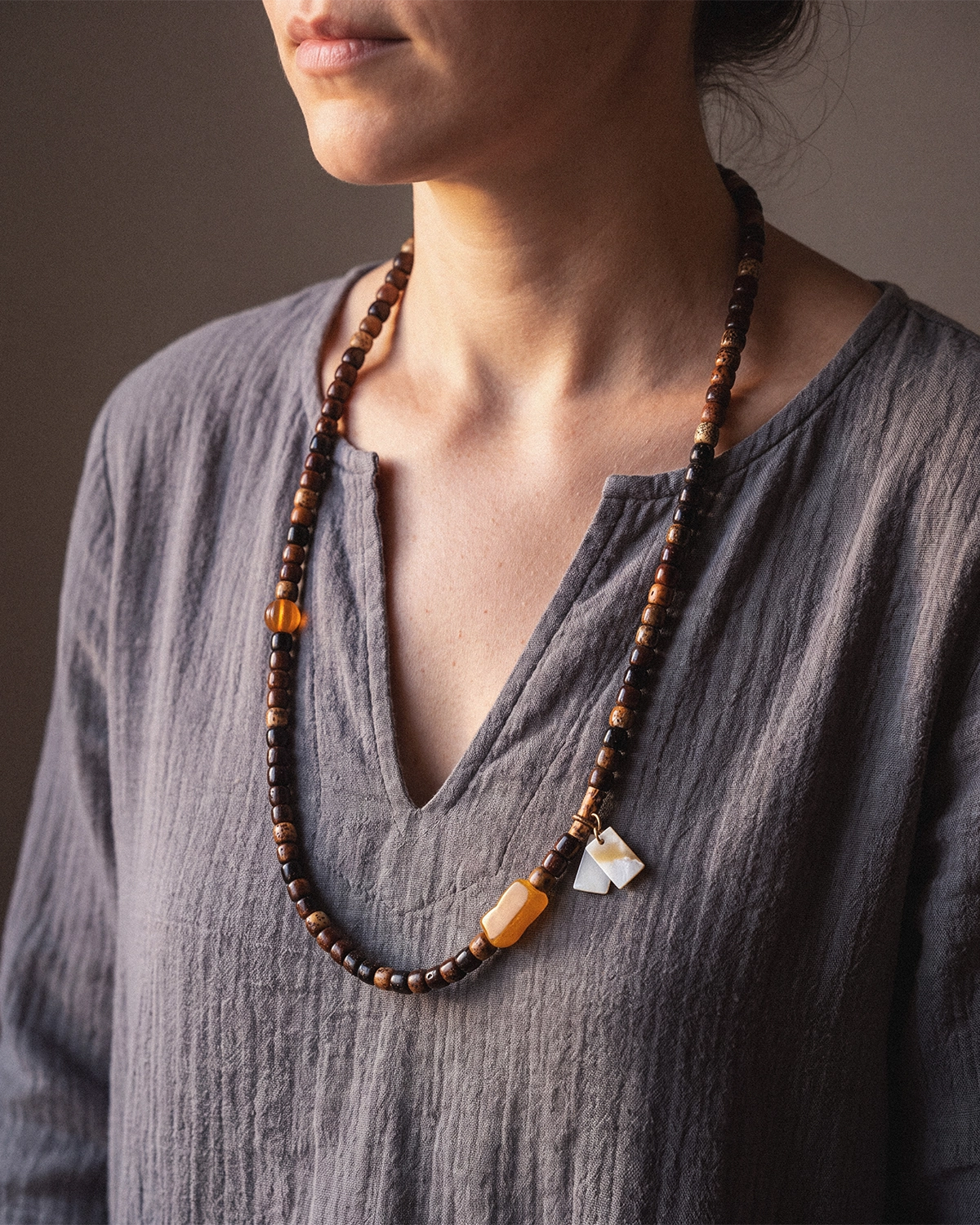 Star and moon bodhi seed mala worn long across a woman's chest, with a gray linen top visible and a shell charm near the lower beads.
