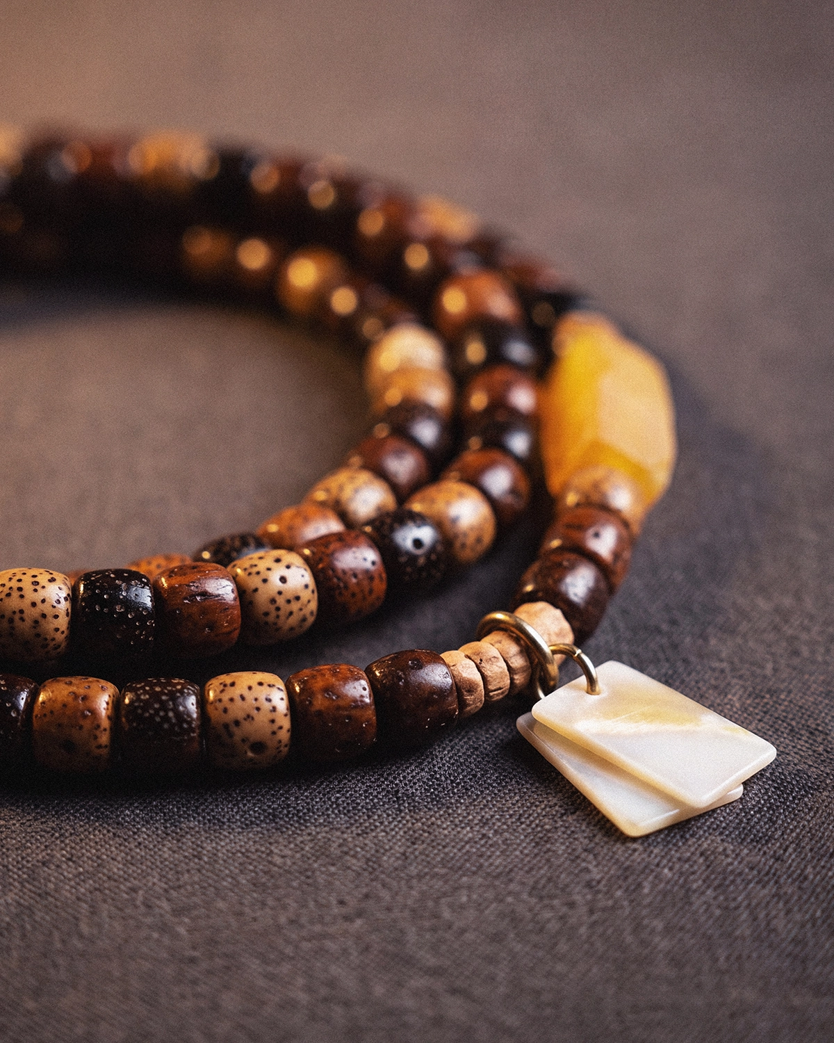 Close-up of star and moon bodhi seed beads with a pale shell pendant hanging from a fine metal ring against dark linen.