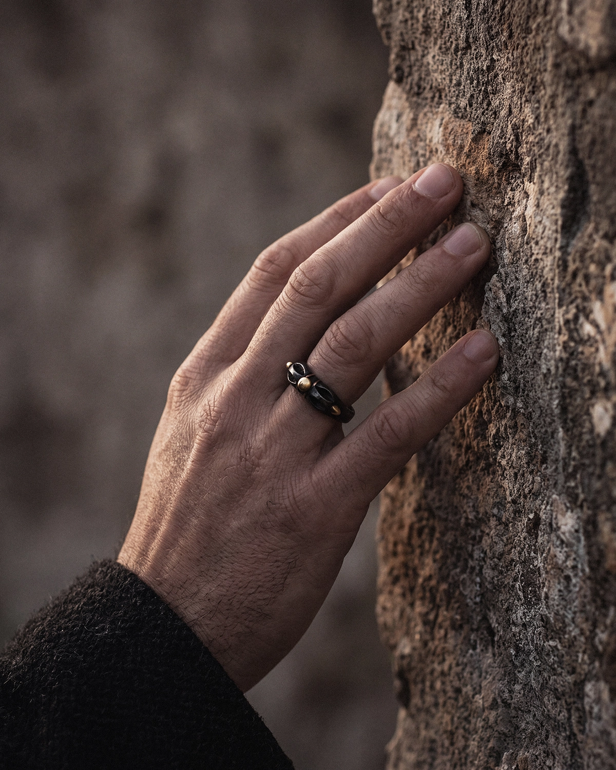 Cold Iron Vajra Dorje ring worn on a relaxed hand resting against a rough stone surface.