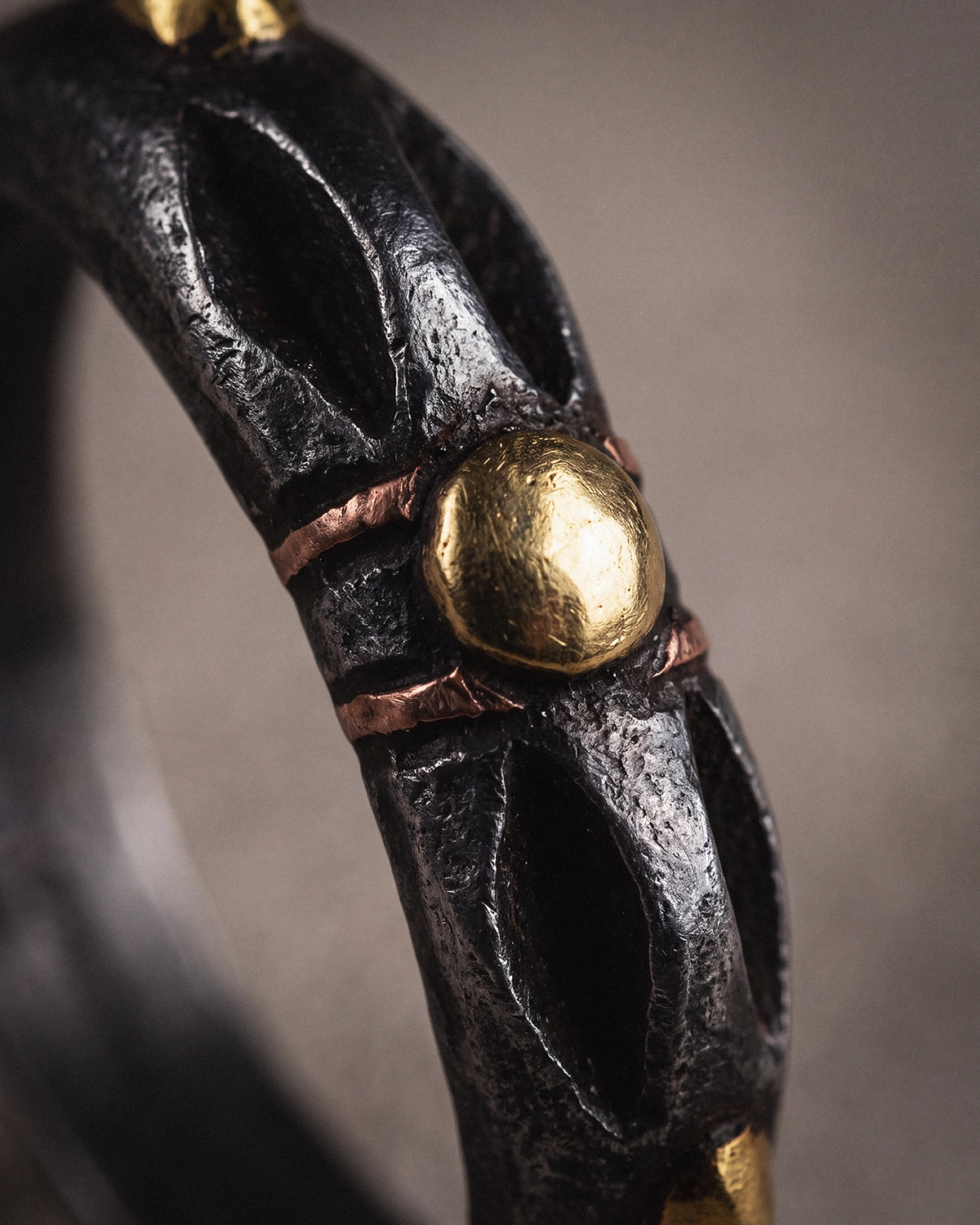Close-up of a Cold Iron Vajra Dorje ring showing gold-toned and copper-toned inlay details against dark textured metal.
