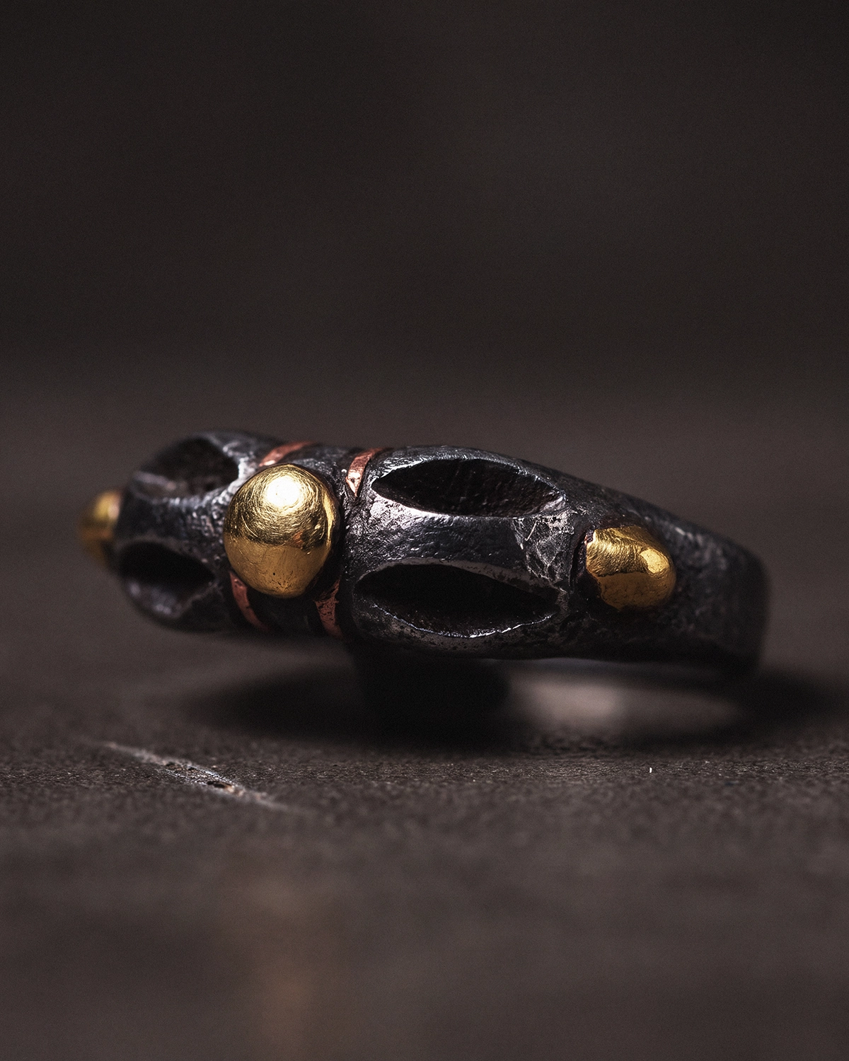 Side view of a Cold Iron Vajra Dorje ring resting on a dark surface, showing its openwork band and inlay accents.